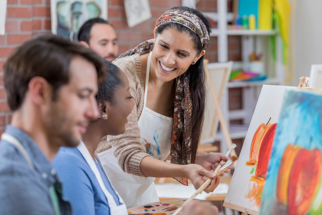A woman teaching a painting class and talking with two other individuals