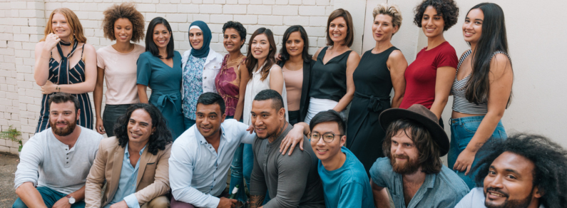 About 20 diverse colleagues pose together for a photograph; some are kneeling and some have their arms around others’ shoulders.