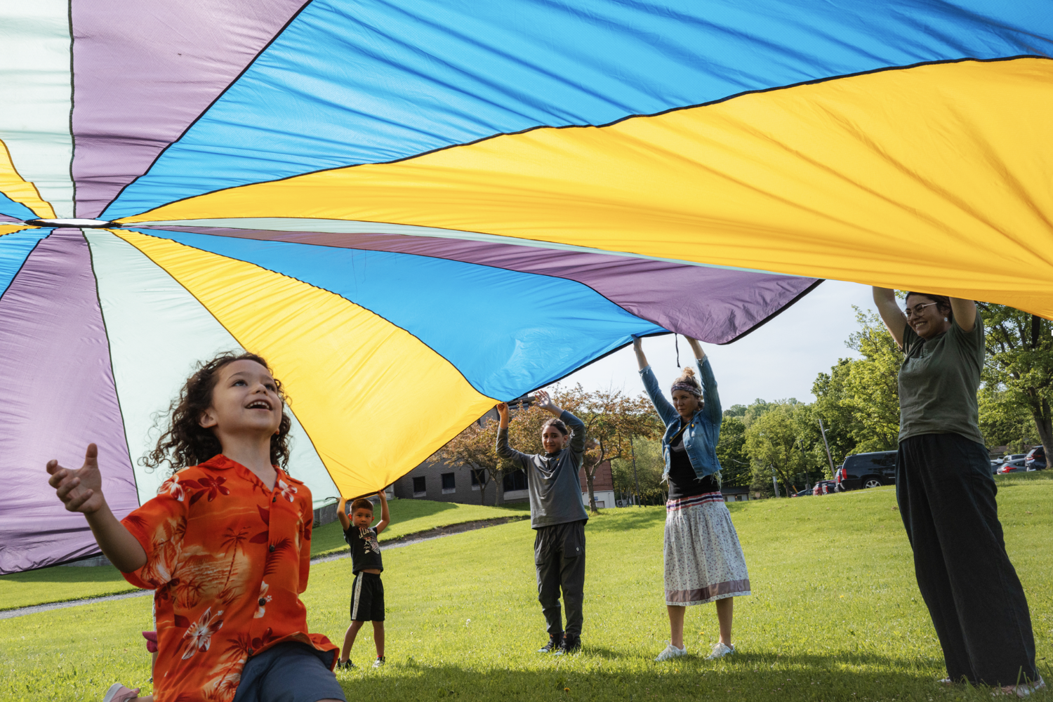 A group of people playing with a colorful parachute and smiling.
